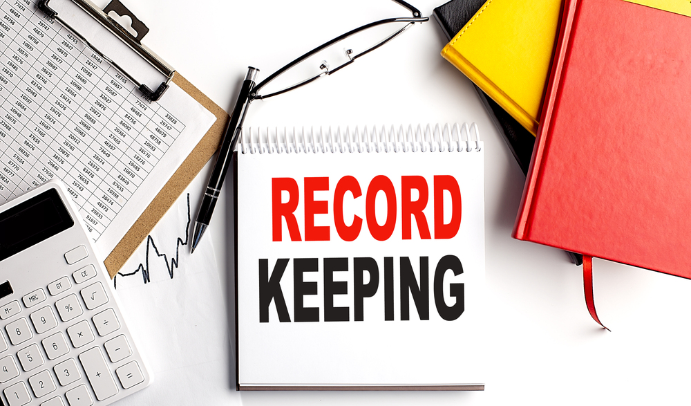 RECORD KEEPING text on notebook with clipboard and calculator on white background